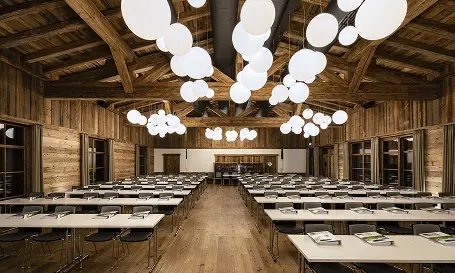 Das Weitblick Allgäu Großer rustikaler Seminarraum mit Holzbalken, langen Tischen und moderner Beleuchtung im alpinen Stil